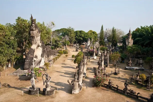 Ein Blick von oben auf einen Skulpturenpark mit einem riesigen liegenden Buddha und vielen weiteren zwischen Bäumen verteilten Statuen.
