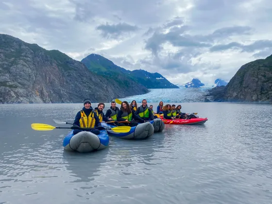 Eine WeRoad Gruppenreise beim Kajakfahren auf einem ruhigen See, mit einem großen Gletscher und Bergen in der Ferne.