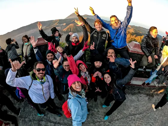 Un grupo de WeRoad posando para una selfie en un mirador, con un gran volcán visible de fondo al amanecer.