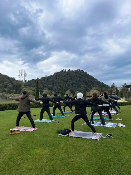 Un viaggio di gruppo WeRoad che pratica una posa yoga su un prato verde con una collina alberata sullo sfondo.