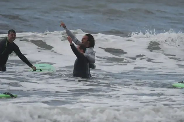 Tre uomini WeRoad in muta sorridono e festeggiano tra le onde spumose dell'oceano con le loro tavole da surf.