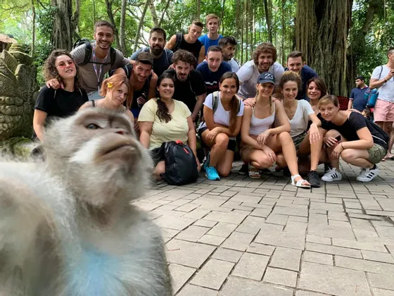 Ein Affe macht ein Nahaufnahme-Selfie mit einer lächelnden und posierenden WeRoad-Gruppe in einem Wald.