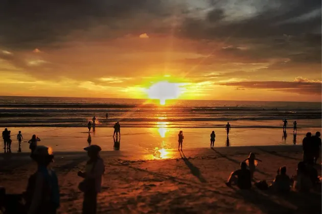 Menschensilhouetten am Strand beobachten einen lebhaften orangefarbenen Sonnenuntergang über dem Meer.