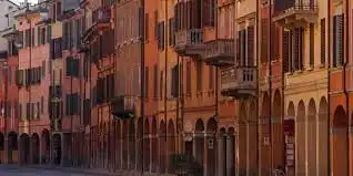 Una strada fiancheggiata da edifici storici a più piani con portici e facciate dai colori caldi.