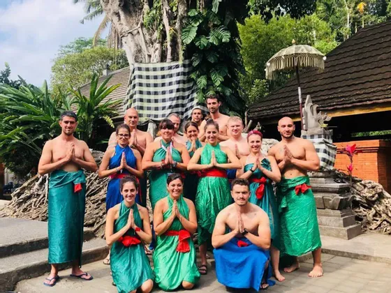 Eine WeRoad-Gruppe trägt farbenfrohe traditionelle Sarongs und posiert mit Händen in Gebetshaltung in einer üppigen, grünen Umgebung.