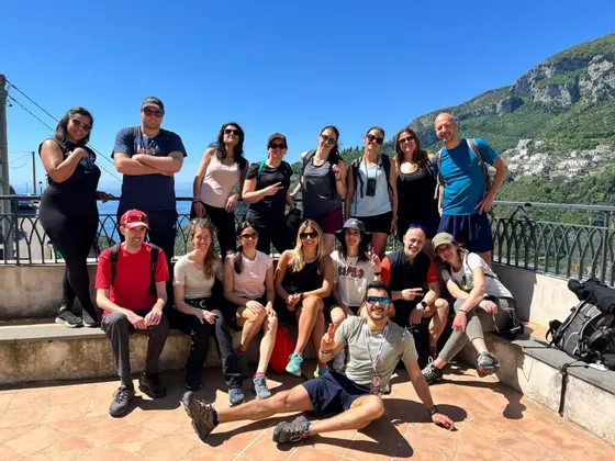 Un grupo de WeRoad posa para una foto en una terraza soleada con vistas a una costa montañosa y al mar.