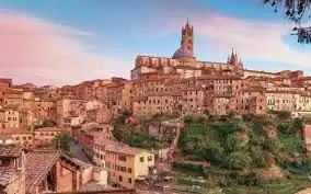 Una città storica costruita su una collina, con una grande cattedrale che domina gli edifici dai tetti in terracotta sotto un cielo dai colori pastello.