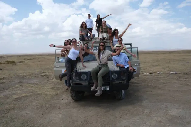 Un gruppo WeRoad sorride e posa per una foto sulla loro jeep da safari in un ampio paesaggio di savana.