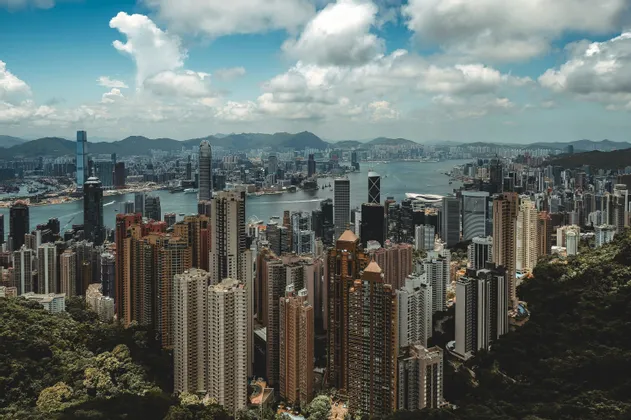 Una vista aerea di una fitta e moderna città con numerosi grattacieli che circondano una baia sotto un cielo nuvoloso.