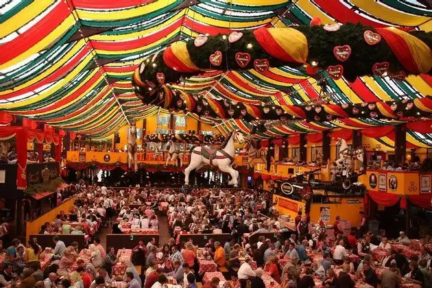 Un tendone festivo affollato, pieno di persone sedute a lunghi tavoli sotto festoni e decorazioni colorate al soffitto.