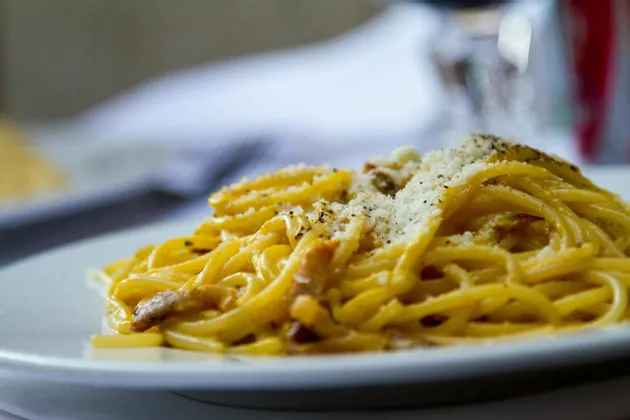 Un primo piano di un piatto di spaghetti alla carbonara, guarnito con formaggio grattugiato e pepe nero.