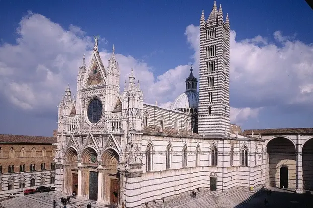 Una cattedrale ornata con un motivo a strisce bianche e scure sulla sua facciata e un alto campanile, vista dall'alto sotto un cielo azzurro.