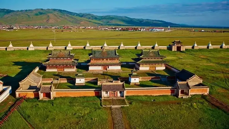 Eine Luftaufnahme eines ummauerten Tempelkomplexes mit traditionellen Gebäuden in einer weiten grünen Ebene, mit einer Stadt und Hügeln in der Ferne.
