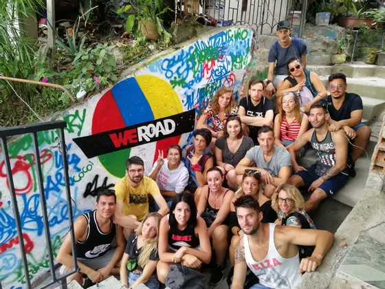 Un gruppo WeRoad in posa per una foto su scale di cemento all'aperto, accanto a un muro con graffiti colorati e un logo WeRoad.