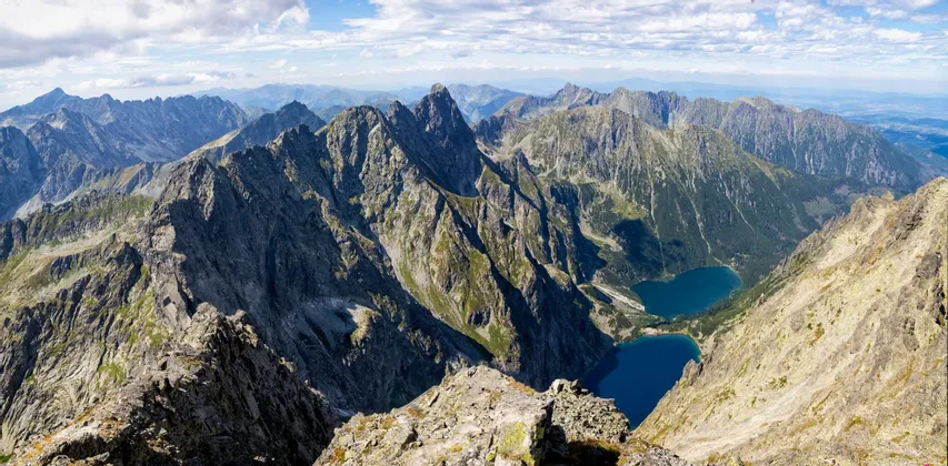 Une vue panoramique depuis un sommet rocheux surplombant une vaste chaîne de montagnes avec deux lacs alpins bleus dans la vallée.