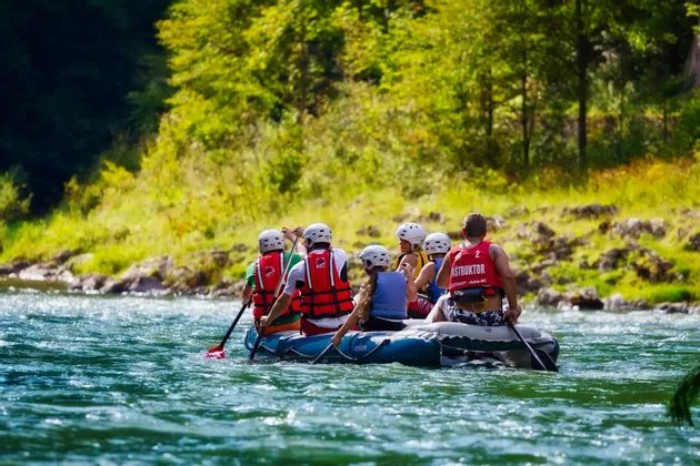 Un groupe WeRoad en rafting sur une rivière, portant casques et gilets de sauvetage, avec une rive arborée en arrière-plan.