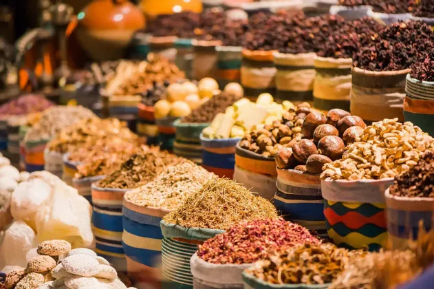 Eine Nahaufnahme verschiedener Gewürze, Kräuter und Nüsse, die in bunten, gestreiften Säcken an einem Marktstand präsentiert werden.