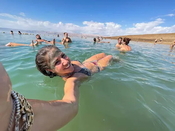 Una donna sorridente con il fango sul viso si fa un selfie mentre galleggia nell'acqua durante un viaggio di gruppo WeRoad.