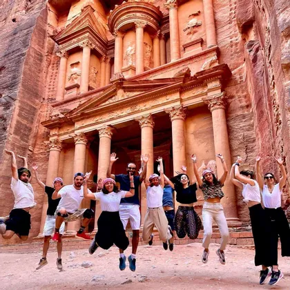 Un viaggio di gruppo WeRoad, con i partecipanti che saltano insieme per una foto davanti a un grande tempio antico scavato in una parete di roccia rossa.
