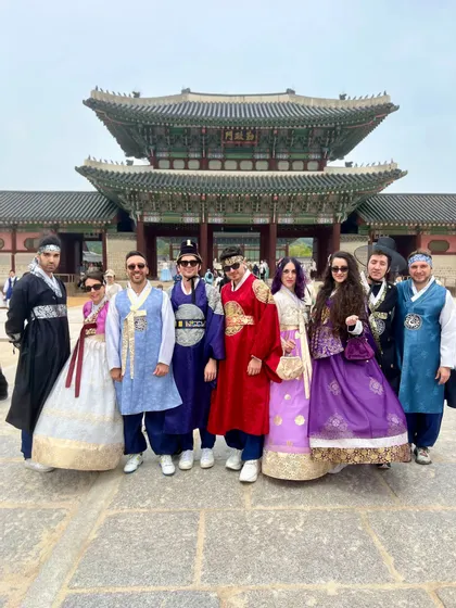 Un viaggio di gruppo WeRoad in posa con colorati abiti tradizionali coreani davanti a un grande cancello tradizionale di un palazzo asiatico.
