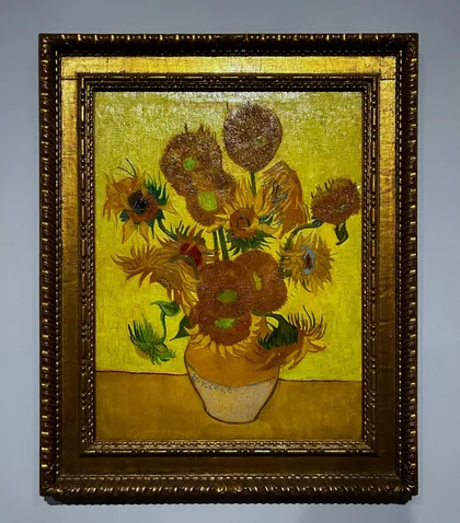 Vincent van Goghs Gemälde 'Sonnenblumen' in einem verzierten, vergoldeten Rahmen an einer Galeriewand.
