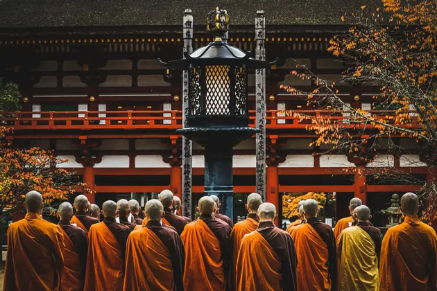 Un gruppo di monaci buddisti in tuniche arancioni si trova di fronte a un tradizionale tempio rosso durante l'autunno.