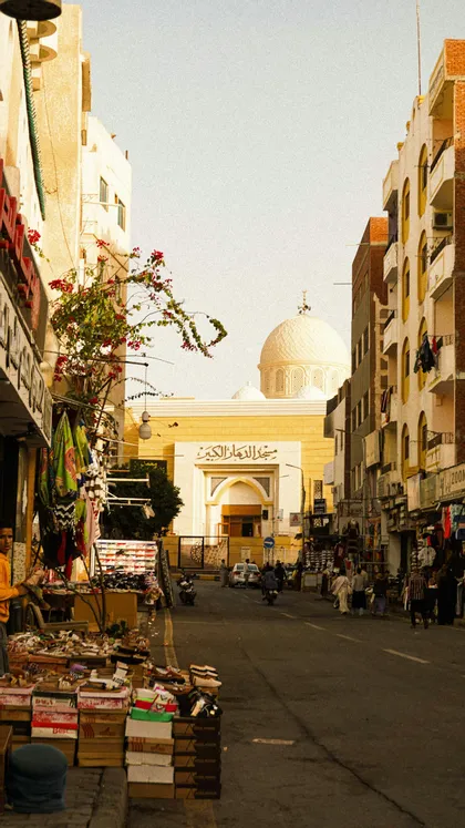 Una vista su una strada cittadina fiancheggiata da negozi, con una moschea prominente e la sua grande cupola bianca visibile sullo sfondo.