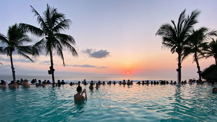 Un viaggio di gruppo WeRoad osserva il tramonto da una piscina a sfioro con vista sull'oceano, incorniciata da palme.