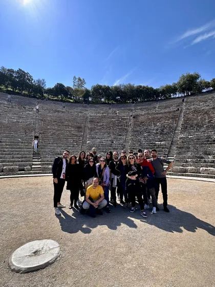 Un gruppo WeRoad posa per una foto al centro di un grande anfiteatro in pietra sotto un cielo azzurro.