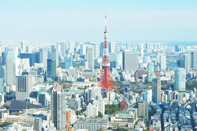 Vue aérienne d'une tour en treillis rouge et blanc au centre d'un paysage urbain dense avec de nombreux gratte-ciel.