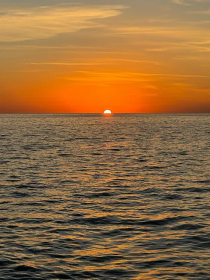 Il sole che tramonta sull'oceano, creando un intenso bagliore arancione sull'acqua e nel cielo.