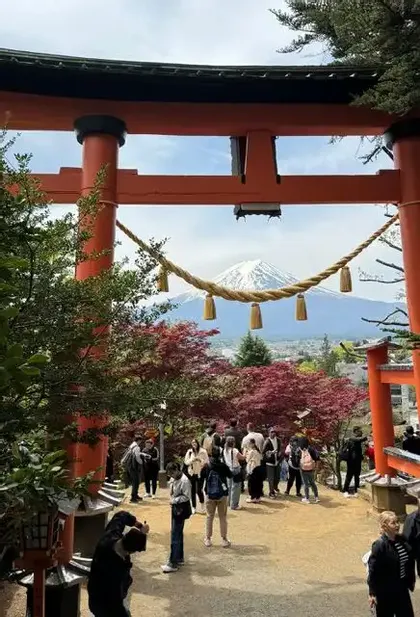 Un viaggio di gruppo WeRoad si riunisce sotto un grande cancello torii rosso per ammirare una montagna innevata in lontananza.