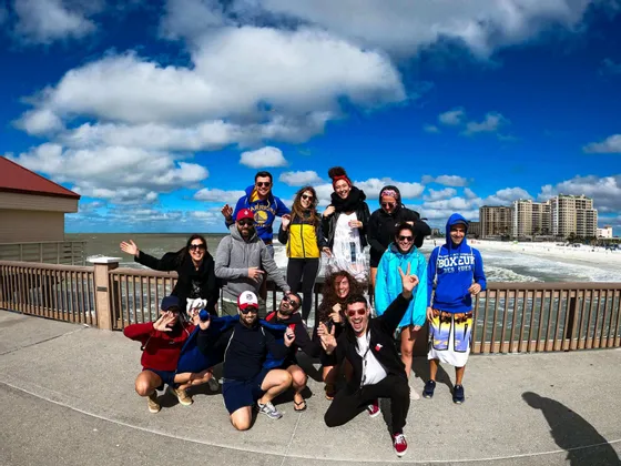 Un gruppo WeRoad in viaggio posa per una foto su un molo, con l'oceano e una spiaggia sabbiosa sullo sfondo.
