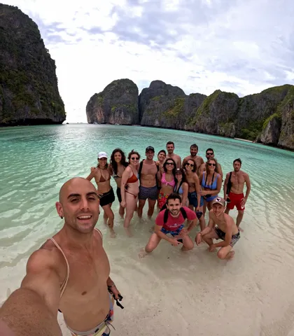 Un homme prend un selfie de son voyage de groupe WeRoad, debout dans l'eau peu profonde et claire d'une baie tropicale entourée de falaises.