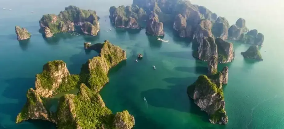 Vista aerea di numerose isole calcaree dalle cime verdi che si ergono da acque calme e turchesi, con piccole barche che navigano tra di esse.