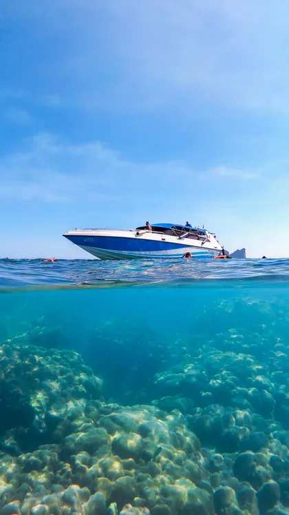 Una vista split-shot di un motoscafo in superficie e di un gruppo WeRoad che fa snorkeling su una barriera corallina.