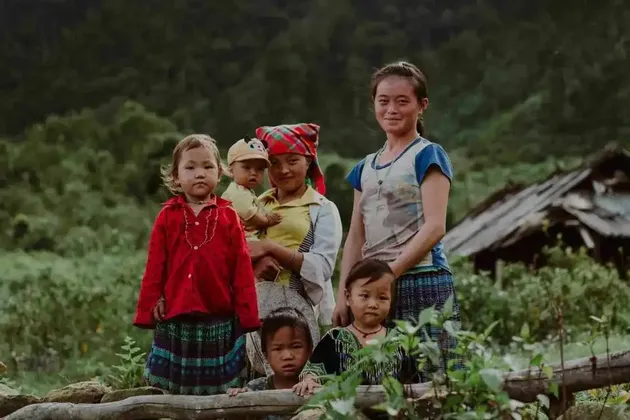 Un gruppo di donne e bambini in abiti colorati posano insieme per una foto in un paesaggio rurale lussureggiante e verde.