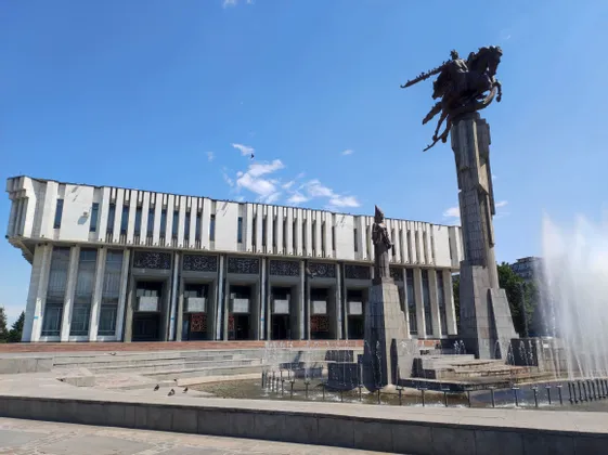 Una estatua ecuestre monumental y una fuente en una plaza frente a un gran edificio blanco bajo un cielo azul claro.