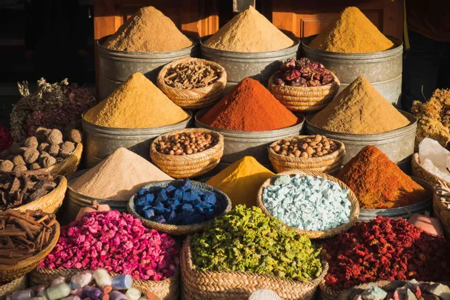 Bunte pulverisierte Gewürze und Trockenwaren, in Haufen und geflochtenen Körben an einem Marktstand im Freien.