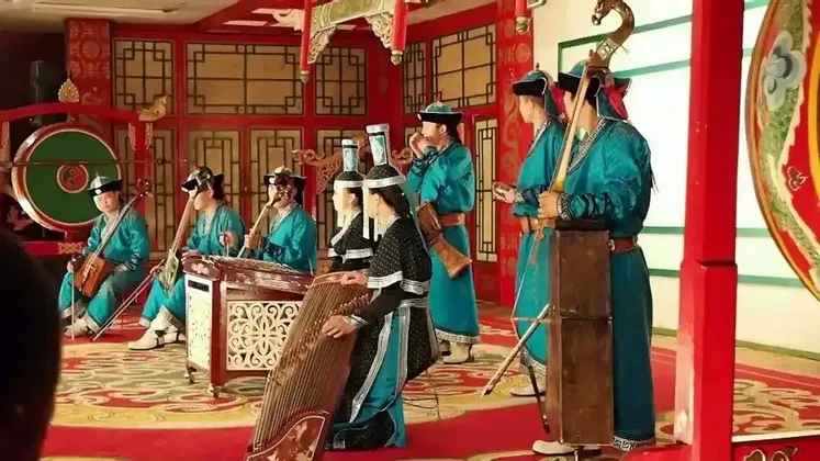 Eine Gruppe von Musikern in traditioneller mongolischer Kleidung spielt verschiedene Saiten- und Schlaginstrumente auf einer farbenfrohen, verzierten Bühne.