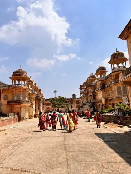 Un viaggio di gruppo WeRoad attraversa una piazza storica fiancheggiata da tradizionali e ornati edifici indiani sotto un cielo blu.