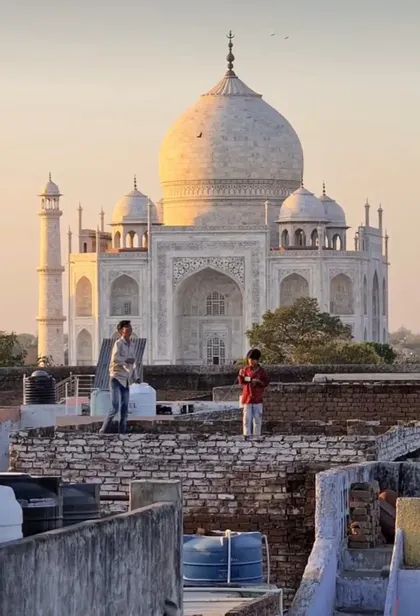 Due ragazzi su un tetto fanno volare aquiloni con il Taj Mahal sullo sfondo al tramonto.