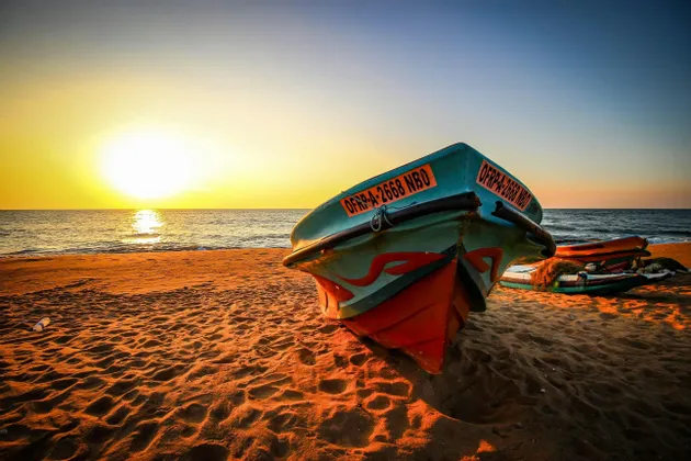 Una barca da pesca colorata riposa su una spiaggia sabbiosa mentre il sole tramonta sull'oceano, proiettando una calda luce dorata.