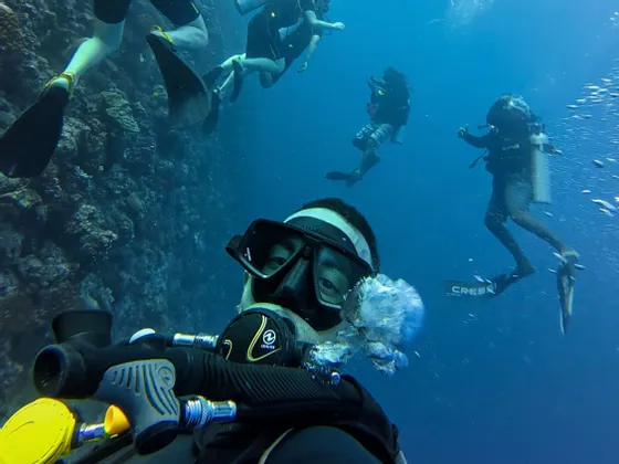 A scuba diver in full gear takes an underwater selfie with their WeRoad group trip swimming nearby.