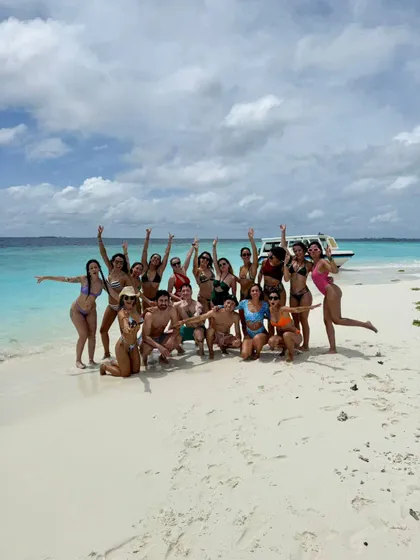 Un viaje en grupo de WeRoad posando para una foto en una playa de arena blanca con agua turquesa y un barco al fondo.
