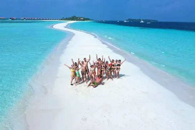 Un viaje en grupo de WeRoad posando en un banco de arena blanca que se curva a través de agua turquesa bajo un cielo azul.