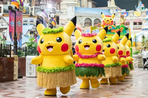 Una fila di persone in costume da Pikachu che indossano gonne di paglia e lei in stile hawaiano sfilano in parata.