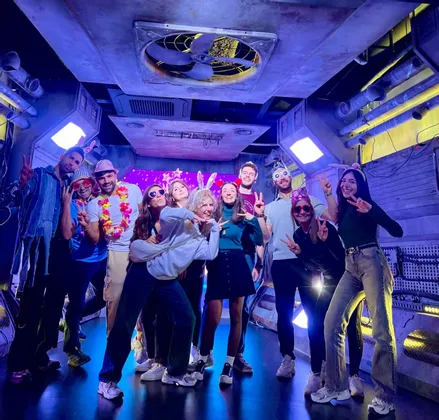 Un viaggio di gruppo WeRoad con persone che sorridono e posano con accessori da festa in una stanza a tema futuristico con luci blu.