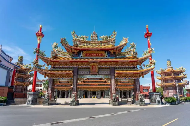 Un grande e ornato portale di un tempio dell'Asia orientale, con un tetto colorato e dettagliato, si erge al di là di una strada sotto un cielo azzurro e limpido.