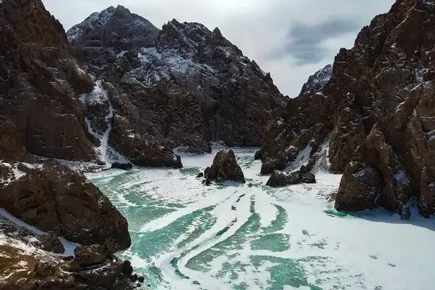 Un río congelado con parches de hielo turquesa serpentea por un cañón rocoso empinado y cubierto de nieve.